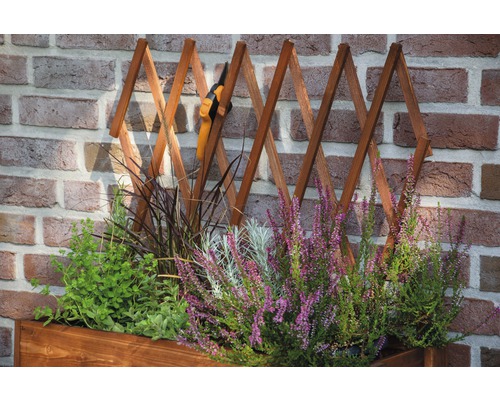 Blumenkasten mit Rankgitter und Gartenschere vor einer Backsteinmauer