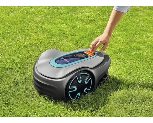 Gardena Mähroboter auf Rasen mit Hand auf Bedienfeld