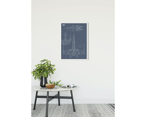 Dekoratives Bild mit einem Schema des X-Wing Raumschiffs im weißen Rahmen über einem Tisch.