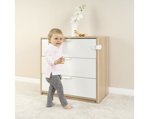 Kindersicherung an einer Kommode mit Schubladen befestigt, ein Kind steht davor.