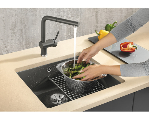 Frau wäscht Salat in einem Küchenspülbecken mit Wasserhahn