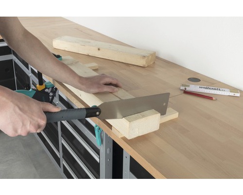 Eine Person sägt ein Holzbrett mit einer Handsäge auf einer Werkbank.