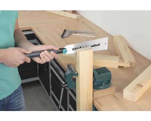 Person sägt Holz mit einer Handsäge an einer Werkbank. Schraubstock hält das Werkstück.
