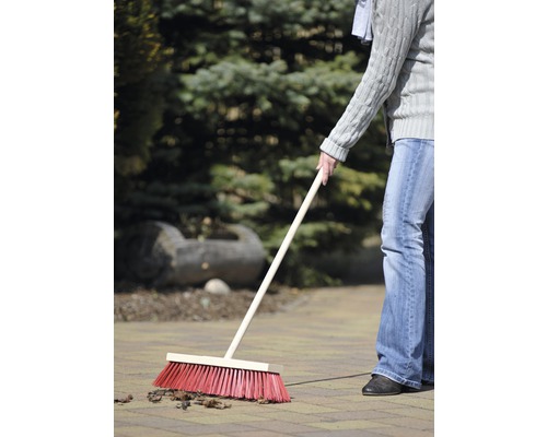 Person kehrt mit einem Straßenbesen Laub auf Pflastersteinen