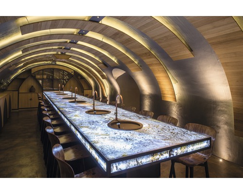 Innenaufnahme eines Raumes mit gewölbter Decke, einem langen Tisch mit eingelassenen Waschbecken und Stühlen