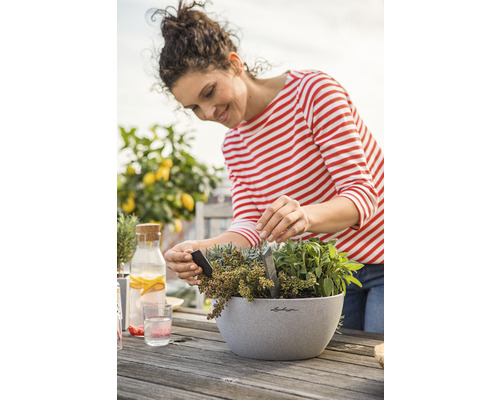Frau pflanzt Kräuter in einen Pflanzkübel auf einem Holztisch