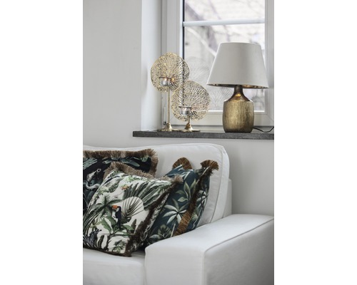Dekoratives Wohnzimmer mit Couch, Kissen mit Dschungelmotiven, Tischlampe und Teelichthaltern