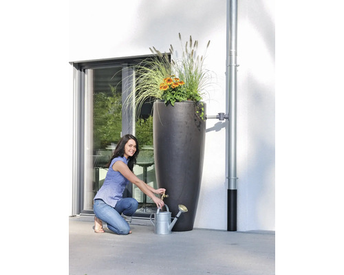 Frau befüllt eine Gießkanne an einer hohen Regentonnen-Säule mit Bepflanzung.