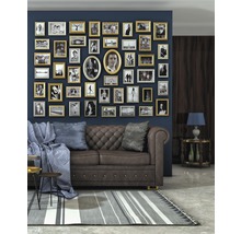 Wohnzimmer mit braunem Sofa, Kissen, Decke, Couchtisch und einer Wand voller Bilderrahmen