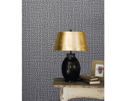 Nahaufnahme einer gemusterten Tapete mit einem Nachttisch, einer Lampe, Büchern und einem Bilderrahmen.