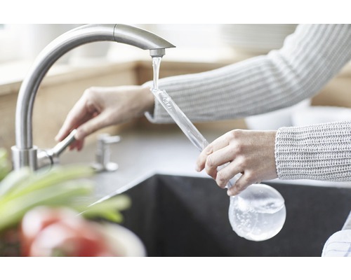 Frau füllt eine Glasflasche am Wasserhahn mit Wasser