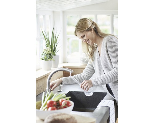 Frau wäscht Gemüse in einer Küchenspüle mit Armatur.