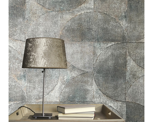 Detailaufnahme einer grauen Zimmerwand mit kreisförmigem Tapetenmuster, einem Tisch mit einer Lampe und Büchern.