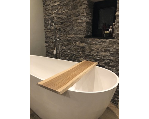 Freistehende Badewanne mit Holzablage in einem Badezimmer mit Steinwand.