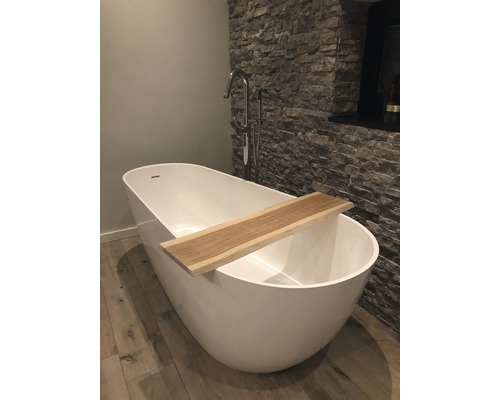 Freistehende Badewanne mit Holzablage und Armatur vor Steinwand