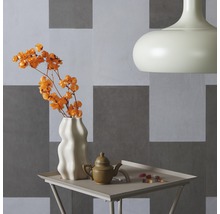 Dekorative Stillleben-Szene mit Blumenvase, Teekanne, Süßigkeiten, Tisch und Lampe vor einer Wand mit quadratischen Mustern.