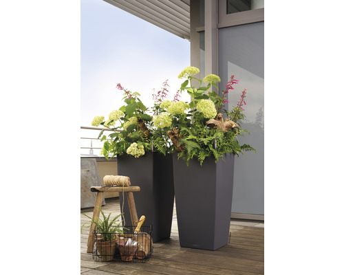 Zwei hohe Pflanzgefäße mit Blumen und Pflanzen auf einem Holzboden.