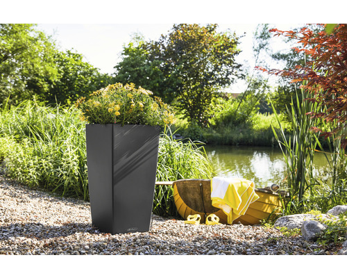Hoher, eckiger Pflanzkübel mit gelben Blumen in einer Gartenszene mit einem Teich