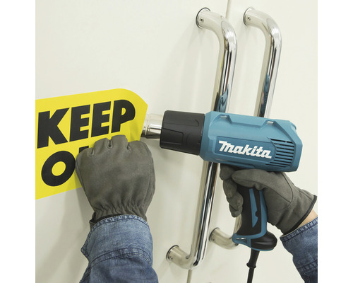 "Eine Person verwendet eine Heißluftpistole der Marke Makita, um ein Schild mit der Aufschrift ""Keep Off"" zu entfernen."