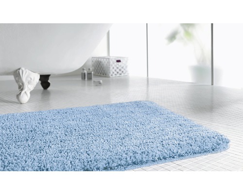 Hellblaue Badematte vor einer Badewanne in einem Badezimmer.