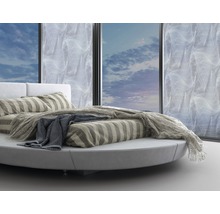 Rundes Bett mit gestreifter Bettwäsche und Tagesdecke vor Fenster