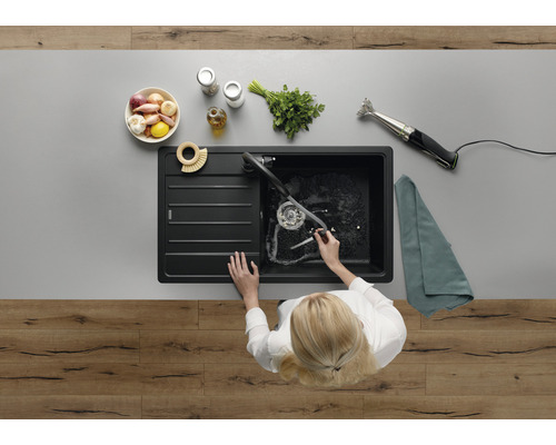 Aufsicht auf eine Person, die in einer schwarzen Küchenspüle Geschirr spült, zusammen mit Lebensmitteln und Küchenutensilien auf der Arbeitsfläche.