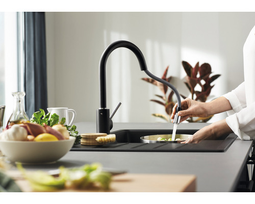 Eine Person spült Gemüse in einem Spülbecken mit einer schwarzen Küchenarmatur.