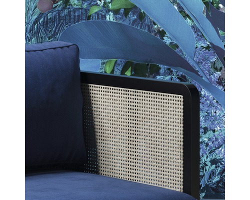 Detailansicht eines blauen Sessels mit Rattanrückenlehne vor floraler Tapete