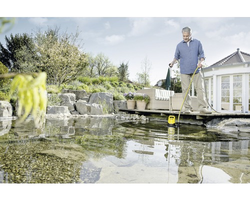 Mann bedient eine gelbe Tauchpumpe im Teich