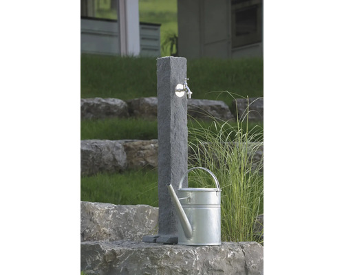 Gartenszene mit Wasserentnahmestelle aus Stein und Gießkanne