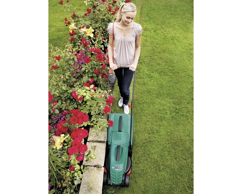 Frau mäht Rasen mit einem elektrischen Rasenmäher im Garten.