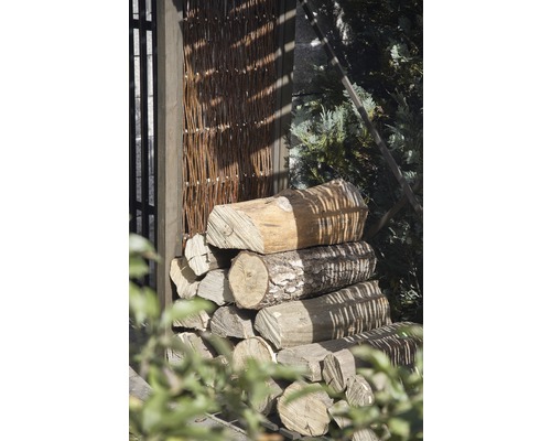 Gestapeltes Brennholz neben einem Zaun aus Weidenholz.