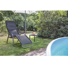 Szene im Garten mit einer Sonnenliege, einem Sonnenschirm und einem kleinen Tisch mit Getränken und einer Wassermelone.