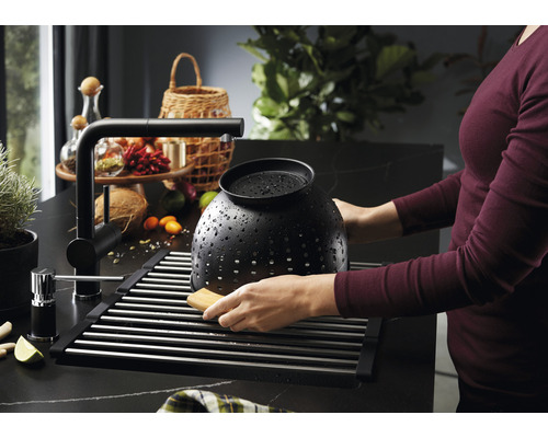 Küchenszene mit Spüle, Abtropfgestell, Armatur und einer Person, die ein Küchensieb spült