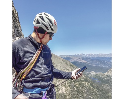 Bergsteiger mit Kletterhelm und Smartphone in Berglandschaft