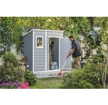 Mann kehrt Blätter vor einem Gerätehaus im Garten.
