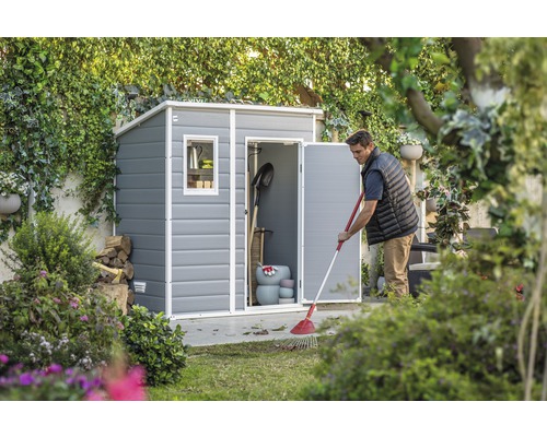 Mann kehrt Blätter vor einem Gerätehaus im Garten.