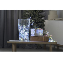 Dekorative Szene mit Glasvase, Lichterkette und Geschenken auf einem Tisch vor einem Weihnachtsbaum