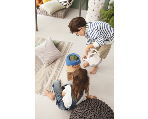 Zwei Kinder im Innenraum, eines gießt eine Pflanze in einem Blumentopf mit Gesicht mit einer Gießkanne.