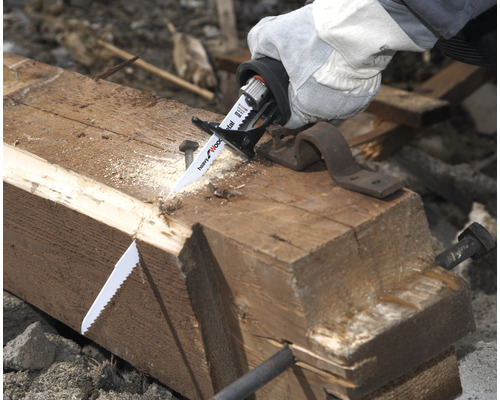 Hand mit Schutzhandschuh beim Sägen eines Holzbalkens mit einer Säbelsäge