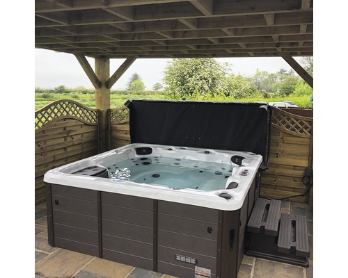 Outdoor Whirlpool mit Abdeckung und Treppe unter einer Holzkonstruktion.