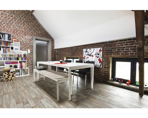 Helles Esszimmer mit Esstisch, Bank, Stühlen und Bücherregal vor Ziegelwand