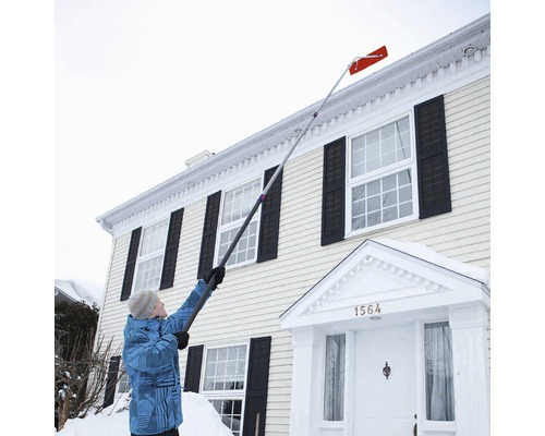 Person entfernt Schnee mit einem Dachrechen vom Dach eines Hauses.