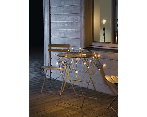 Gartenszene mit Lichterkette auf Tisch und Stühlen auf einer Terrasse