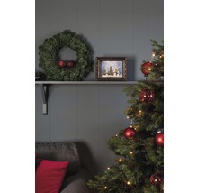 Festlich geschmücktes Wohnzimmer mit Weihnachtsbaum, Kranz und Dekorationen auf einem Regal