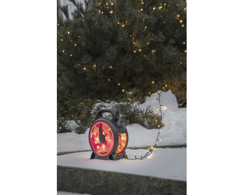 Lichterkette auf Kabeltrommel im Schnee vor einem Baum mit Lichtern