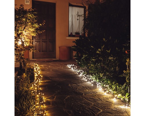 Beleuchteter Gartenweg mit Lichterketten am Abend.