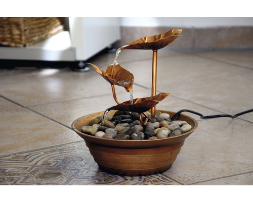 Dekorativer Zimmerbrunnen mit Wasserlauf über Blätter und Steine