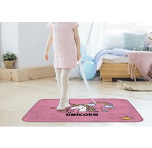 Mädchen steht auf einem pinkfarbenen Teppich mit Einhornmotiv in einem hellen Raum.