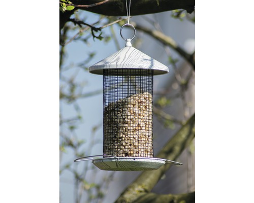 Vogelhaus mit Futternetz und Futter gefüllt hängt an einem Baum.